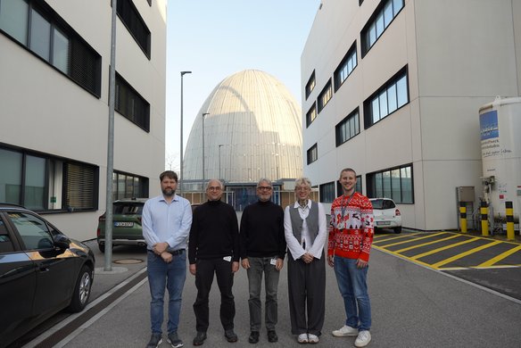 Fünf Personen posieren vor modernen Institutsgebäuden und der markanten Atom-Ei-Kuppel in Garching.